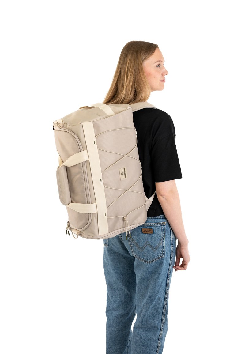 Borsa da viaggio color beige chiaro con tessuto testurizzato, cinghie in fettuccia e corde bungee esterne. Maniglia laterale e chiusura con zip, indossata sulla schiena.