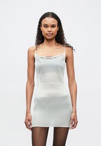 Ανοιχτό γκρι ριγέ πλεκτό φόρεμα με λεπτές τιράντες, που διαθέτει εφαρμοστή ζώνη και κοντό τελείωμα, σε συνδυασμό με διάφανα μαύρα καλσόν.