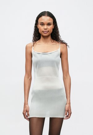 Ljusgrå ribbad klänning med tunna axelband, som har en figurnära överkropp och en kortare nederdel, kombinerad med genomskinliga svarta strumpbyxor.