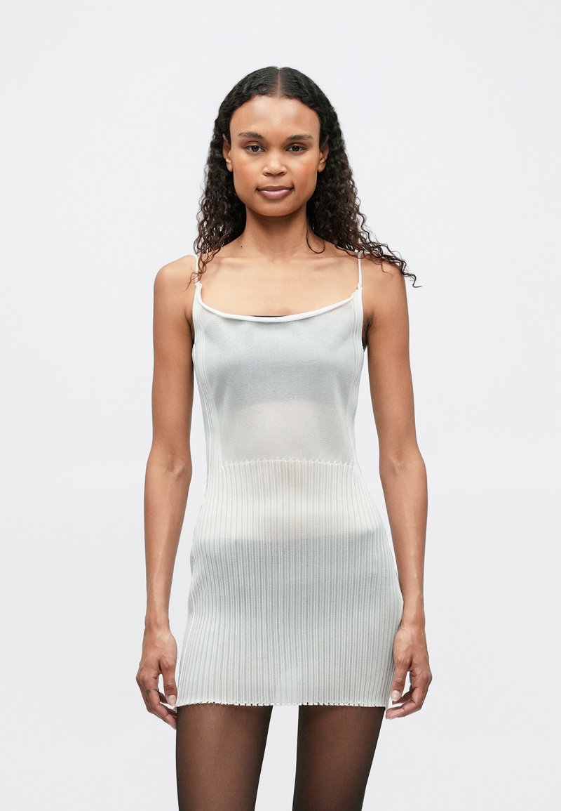 Ανοιχτό γκρι ριγέ πλεκτό φόρεμα με λεπτές τιράντες, που διαθέτει εφαρμοστή ζώνη και κοντό τελείωμα, σε συνδυασμό με διάφανα μαύρα καλσόν.