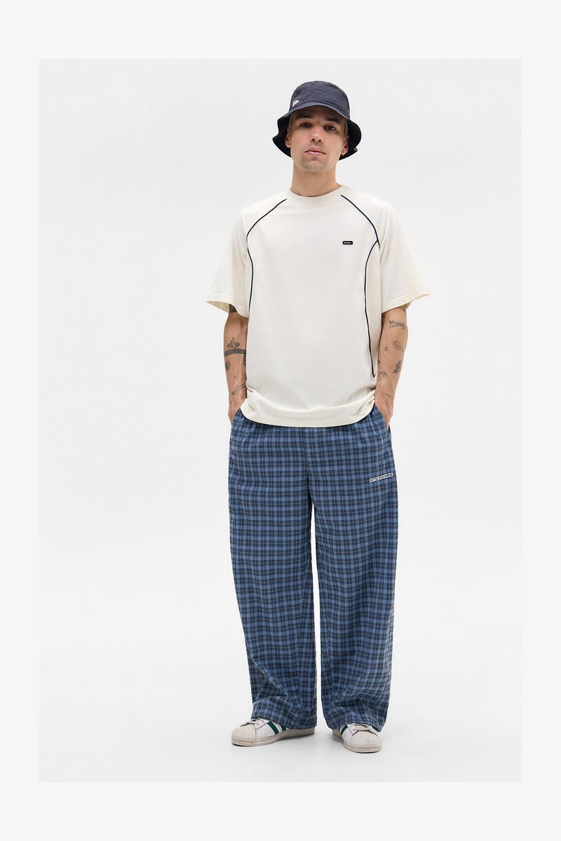 T-shirt in cream with black piping, paired with blue plaid pajama pants. Features a relaxed fit and white sneakers. Bucket hat completes the look.
