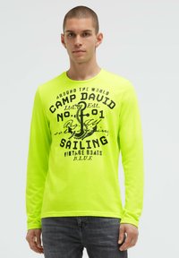 Langärmeliges Neon-Gelb T-Shirt mit schwarzem grafischem Text und Anker-Design. Verfügt über einen Rundhalsausschnitt und eine weiche, glatte Textur.