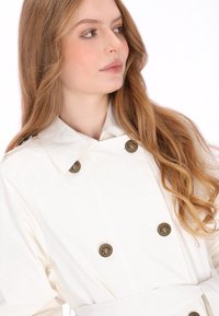 Dubbele rij knopen jas in crèmekleurige stof, met een brede kraag, gouden ankerknopen en een ceintuur die gestrikt is, met een gladde textuur en een nauwsluitende pasvorm.