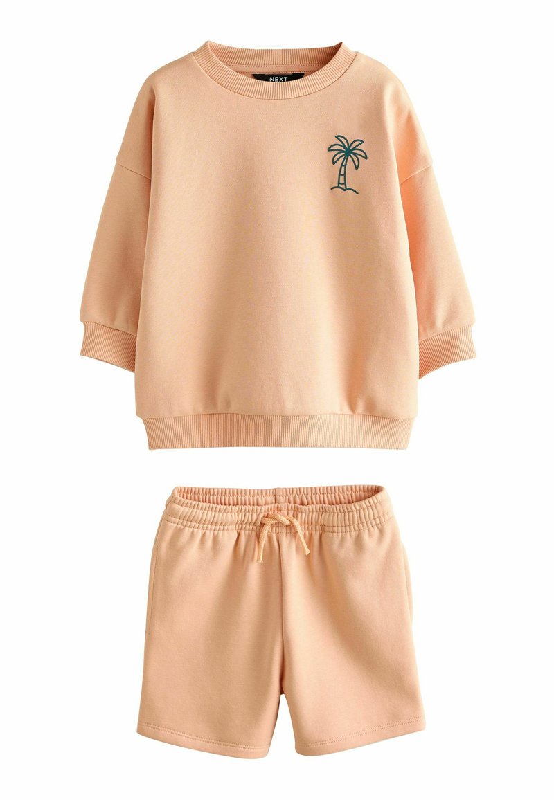 Conjunto de sudadera y pantalones cortos de color melocotón. La sudadera tiene un escote redondo, hombros caídos y un bordado verde de palmera. Los pantalones cortos cuentan con una cintura elástica.