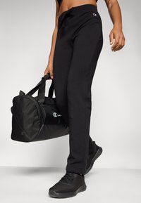 Black cotton sweatpants with a drawstring waistband, worn with a black sports bag, and black sneakers, showcasing a simple, comfortable design.