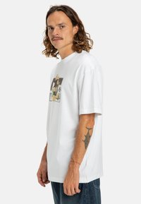 Camiseta de algodón blanca con un diseño gráfico que presenta flores y estrellas en el frente, de mangas cortas y un corte relajado.