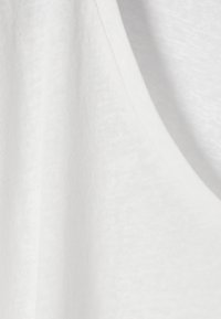 Gros plan sur un tissu blanc doux montrant une texture tricotée et un détail de couture incurvée.