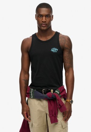 Sort bomulds tanktop med et lyseblåt "SuperDry" logo, parret med cremede cargo shorts og en flerfarvet sweatshirt bundet om livet.
