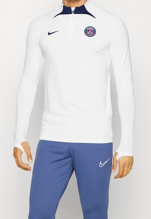 Man wearing white long-sleeve Nike Paris Saint-Germain training top and blue Nike sports pants with thumb holes on sleeves.