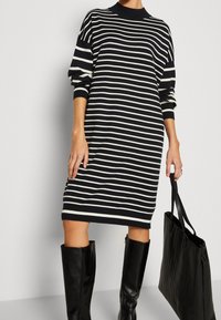 Raidallinen neulemekko, jossa on mustavalkoisia vaakasuoria raidoituksia, ribattu kaulus ja hihansuut, sekä polvipituinen malli, yhdistettynä mustaan olkalaukkumaan.