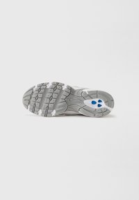 Gray athletic shoe sole featuring textured rubber material, hexagon and oval tread patterns, with blue and white accents.