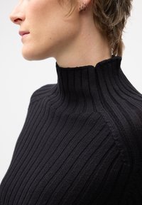 Pull turtleneck en tricot côtelé noir avec un col haut, un tissu texturé et des coutures le long des épaules.