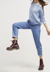 Pull en rayures bleu clair à manches longues, associé à un chino bleu clair retroussé et des bottes bordeaux à lacets avec des semelles épaisses.