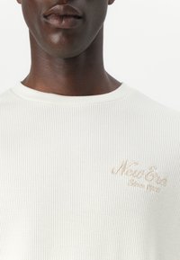 Krém színű bordázott rövid ujjú póló kerek nyakkivágással, bal mellrészen finom bézs hímzett "New Era" logóval.