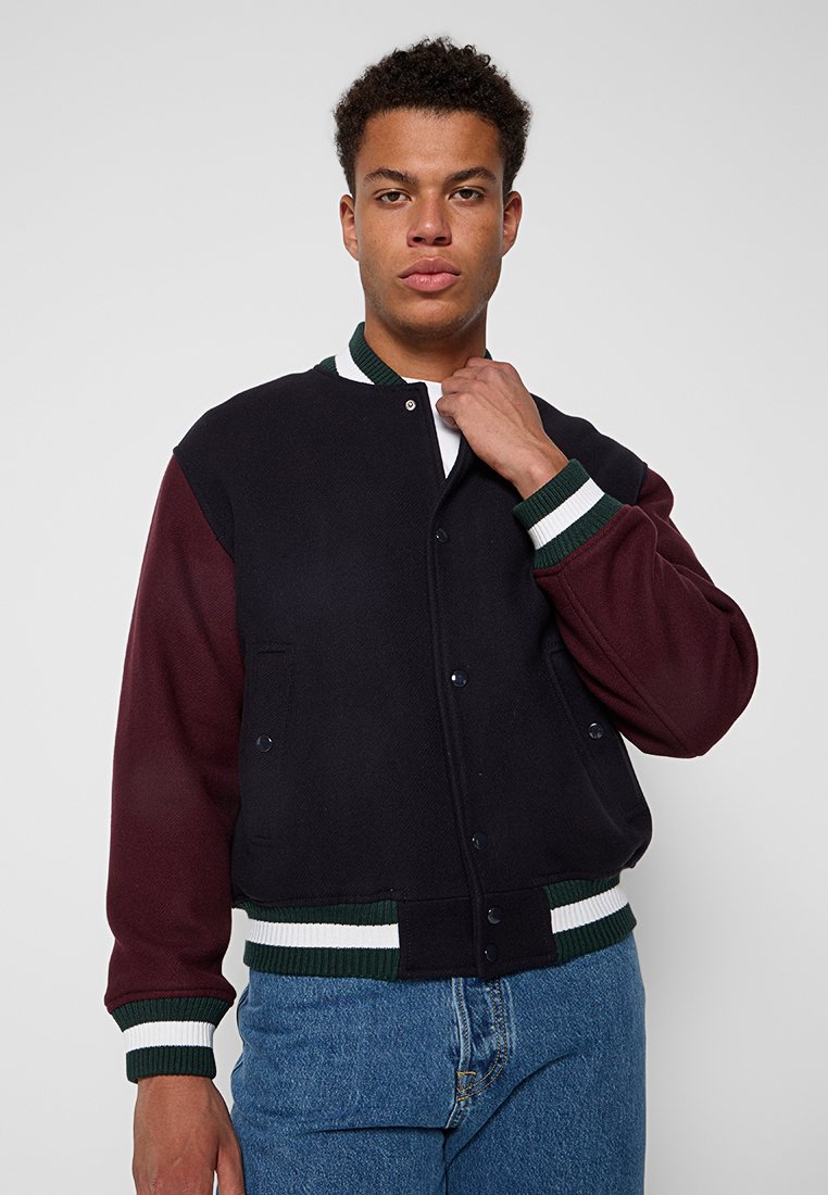 Veste varsity noire et bordeaux avec boutons pression, poignets en maille verte et blanche, et coupe décontractée, fabriquée en tissu texturé.