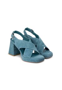 Sandalias de tacón alto de ante en color verde azulado, con tacón cuadrado, diseño de correas cruzadas y hebilla ajustable en el tobillo. Punta cuadrada y superficie texturizada.