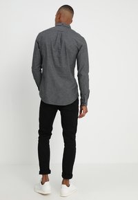 Grijs shirt met lange mouwen, een plooi aan de achterkant, knopen aan de manchetten en een afgeronde zoom, gecombineerd met zwarte slim-fit broek en witte sneakers.