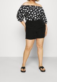 Czarna bluzka z odkrytymi ramionami ozdobiona białymi wzorami liści, w połączeniu z czarnymi szortami. Dopełnieniem stroju są płaskie czarne klapki.