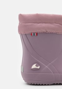 Bota de goma morada con un puño de tela, que presenta un pequeño logo y un acento tricolor. Textura suave con una suela estriada para mayor tracción.