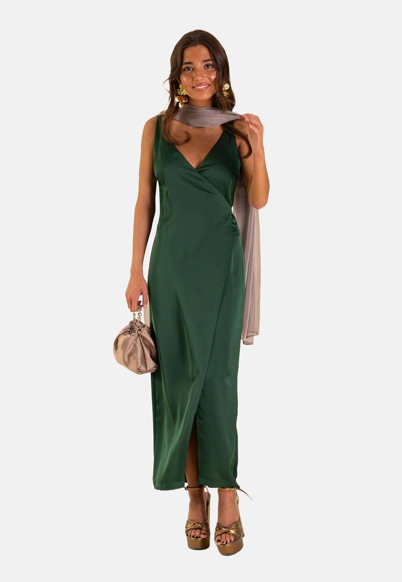 Vestido de satén verde con un escote pronunciado y una abertura alta. Combinado con una bufanda beige y un clutch topo, usado con tacones de plataforma.