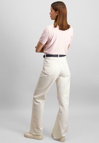 Jasnoróżowa koszulka z krótkim rękawem w połączeniu z wysokimi spodniami z szerokimi nogawkami w kolorze kremowym. Pleciony granatowy pasek, białe sneakersy, gładka faktura materiału.