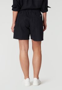Pantalones cortos de lino azul marino oscuro con cintura elástica, bolsillos laterales y traseros, combinados con zapatillas blancas, tomados desde atrás.