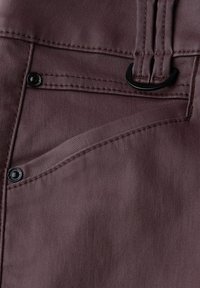 Tela de color malva oscuro con un bolsillo de hardware negro y costuras. Superficie suave con un brillo sutil y un detalle de línea curva en el bolsillo.