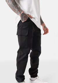 Zwarte cargobroek met meerdere zakken, elastische boorden en een slim fit. Gemaakt van duurzaam materiaal met een matte textuur.