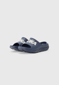 Marinblå slide-sandaler med öppen tå-design, gjorda av ett glättat material, med en vit logotyp och en texturerad gummisula för bättre grepp.