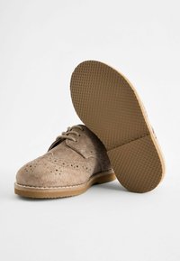 Chaussures en daim brun clair avec des détails perforés et un design à lacets. Semelle en caoutchouc épaisse et texturée avec un bord lisse.