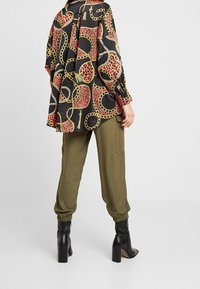 Langarmbluse mit schwarzem Grund und buntem Muster aus Kette und Leopardenfleck; kombiniert mit olivgrünen Cargo-Hosen und Stiefeletten mit Absatz.