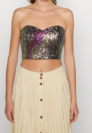 Mujer que lleva un crop top sin tirantes de pedrería multicolor y una falda plisada crema de cintura alta con botones delanteros.