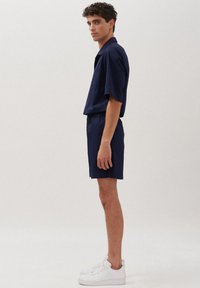 Marineblauw shirt met korte mouwen en bijpassende shorts, gemaakt van zacht materiaal. Heeft een ontspannen pasvorm en een eenvoudig ontwerp, gecombineerd met witte sneakers.