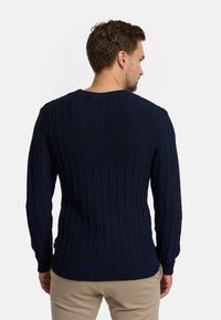 Marineblauwe ribgebreide trui met lange mouwen en een ronde hals. Kenmerkt zich door een gestructureerd patroon en een aansluitende pasvorm.