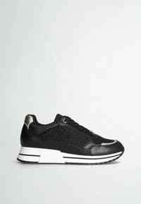 Baskets noires avec côtés en mesh, semelle blanche à rayures noires et accents argentés métalliques au talon et à l’orteil sur fond clair uni.