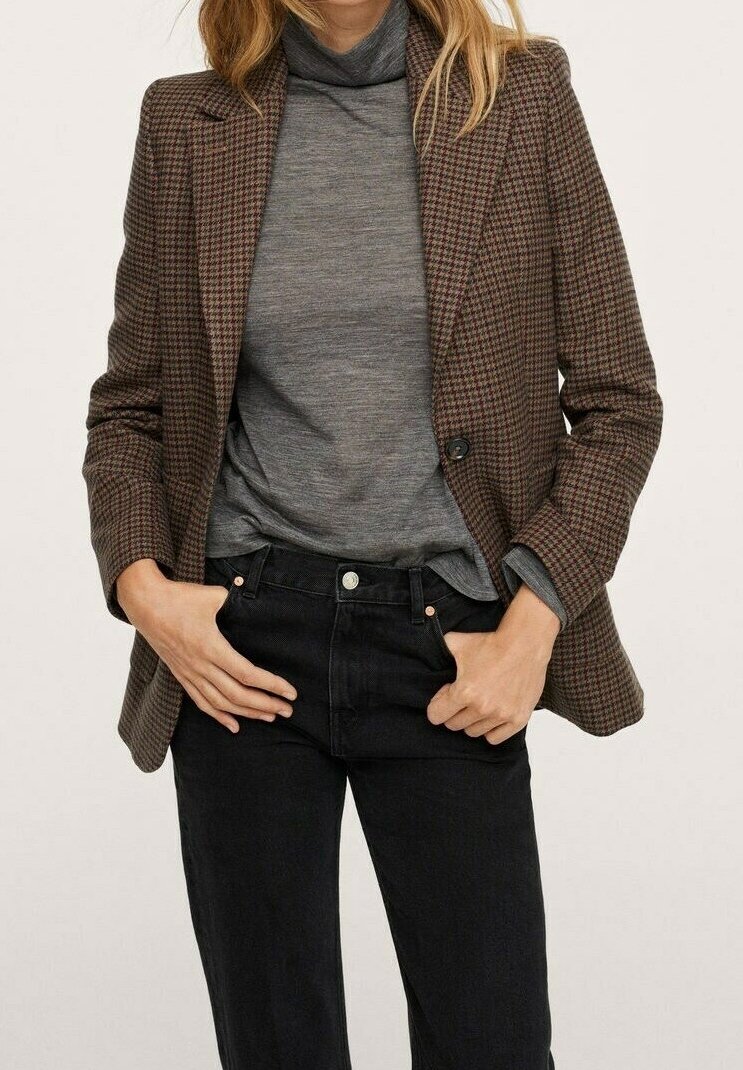 Blazer de cuadros marrones con un diseño estructurado, cierre de un solo botón, llevado sobre un suéter de cuello alto gris y combinado con jeans negros.
