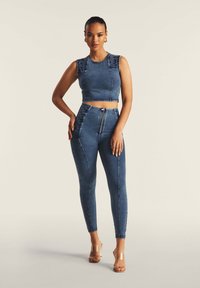 Denim crop top dengan aksen bahu berkerut dan celana jeans high-waisted yang dilengkapi penutup ritsleting serta jahitan kaki dalam warna biru sedang.