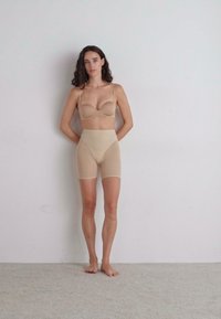 Nude brezšiven modrček z nastavljivimi naramnicami in visokimi oblikovalkami kratkimi hlačami. Gladka tekstura, prilegajoča zasnova, brez vidnih šivov, minimalističen stil.