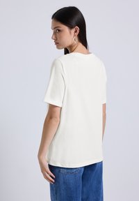 Camiseta blanca de manga corta con un corte relajado y puños enrollados, combinada con unos vaqueros azules de corte holgado, que muestra un material de algodón suave.
