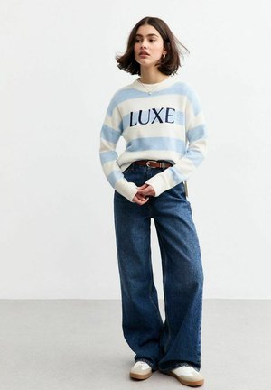 Blauw-wit gestreepte sweater met de tekst "LUXE", gecombineerd met hoge taille wijde blauwe jeans en lichte sneakers. Glad textuur en een casual pasvorm.