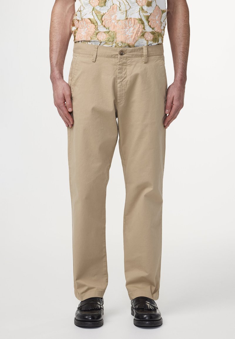 Beige puuvillapuhujad, sirge jala lõikega, nupuväärise ja külgtaskutega, koos mustade loaferitega.