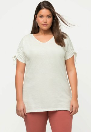 T-shirt bianco a maniche corte con scollatura a v, caratterizzato da dettagli a cravatta sulle maniche. Il tessuto ha una texture morbida. Abbinato a pantaloni rosa.