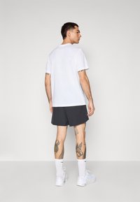 Vit kortärmad t-shirt i kombination med svarta sportshorts. T-shirten har en klassisk passform, medan shortsen är lösa med en slät textur.