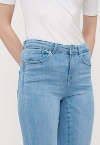 Jeans de mezclilla azul claros con cintura a media altura, diseño de cinco bolsillos y detalles de costura sutiles, combinados con una camiseta blanca lisa.