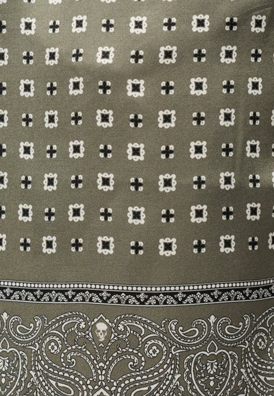 Tissu vert olive avec de petits motifs floraux blancs et motifs géométriques noirs répétitifs, bordé d'un motif ornemental blanc de paisley et de crânes.