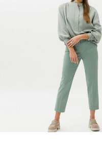 Ljusgrön blus med knappar och hög krage, i kombination med höga ljusgröna byxor. Outfiten har en avslappnad passform och mjukt tyg.