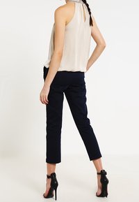 Krämfärgad ärmlös topp med ett nyckelhål baktill, matched med marinblå knälånga byxor och svarta högklackade sandaler.