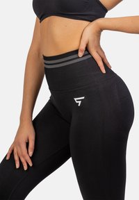 Zwarte high-waisted leggings van textuurstof, met contrasterende grijze strepen op de taille en een wit logo-accent op de dij.