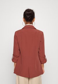 Rostfärgad kavaj med skräddarsydd passform, spetsiga slag och uppvikta ärmar. Tillverkad av ett smidigt tyg med en enda bakre slits.