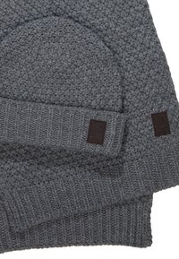 Grå strikket hue og tørklæde sæt. Funktioner teksturerede stikmønstre, ribkant og brune læderlogo-patches.